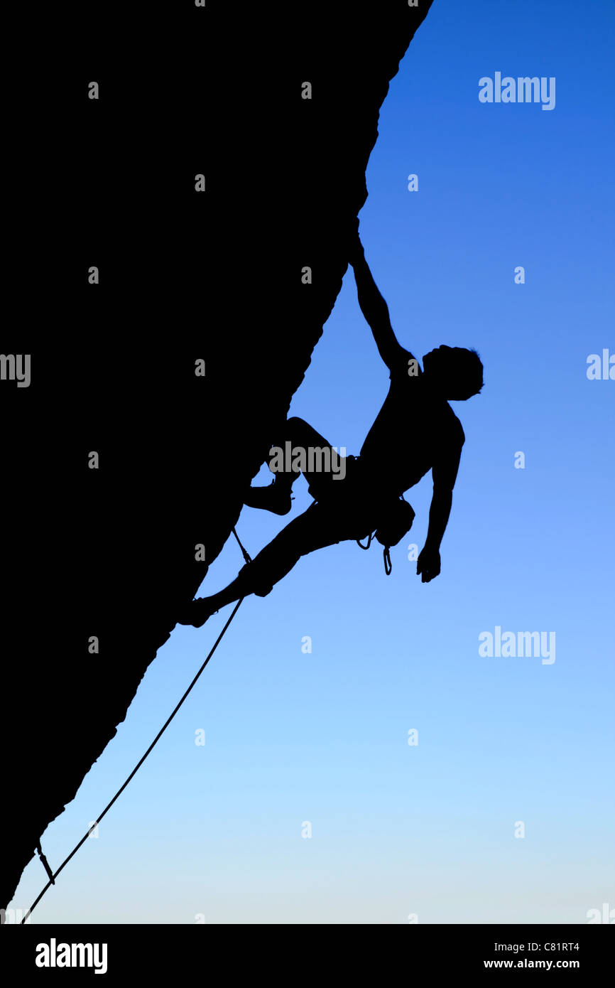 silhouette of rock climber climbing an overhanging cliff with blue sky background Stock Photo