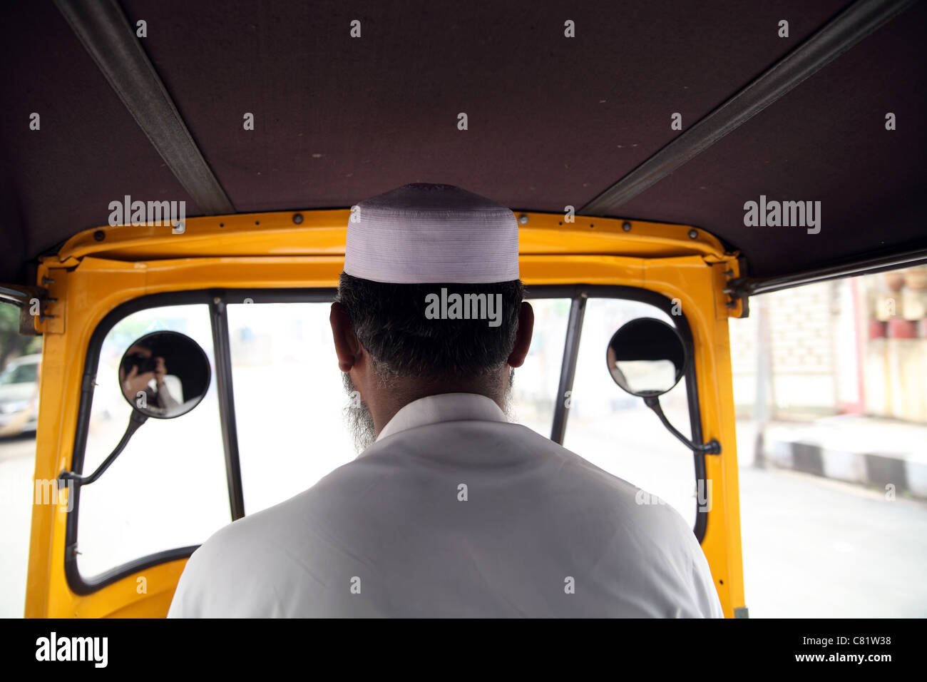 View of back of autorickshaw driver, a Muslim man wearing traditional woven cap,  taken from passenger seat Stock Photo