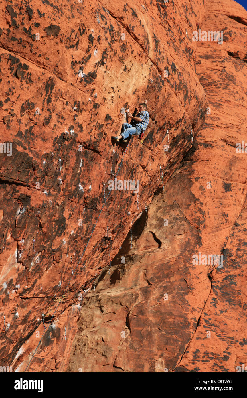 a man in blue rock climbs overhanging red rocks Stock Photo