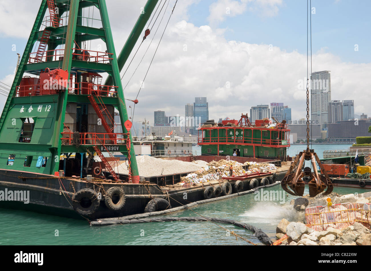 Dredging barge with crane lifting rocks in the land reclamation along Wan Chai waterfront, Hong Kong Stock Photo