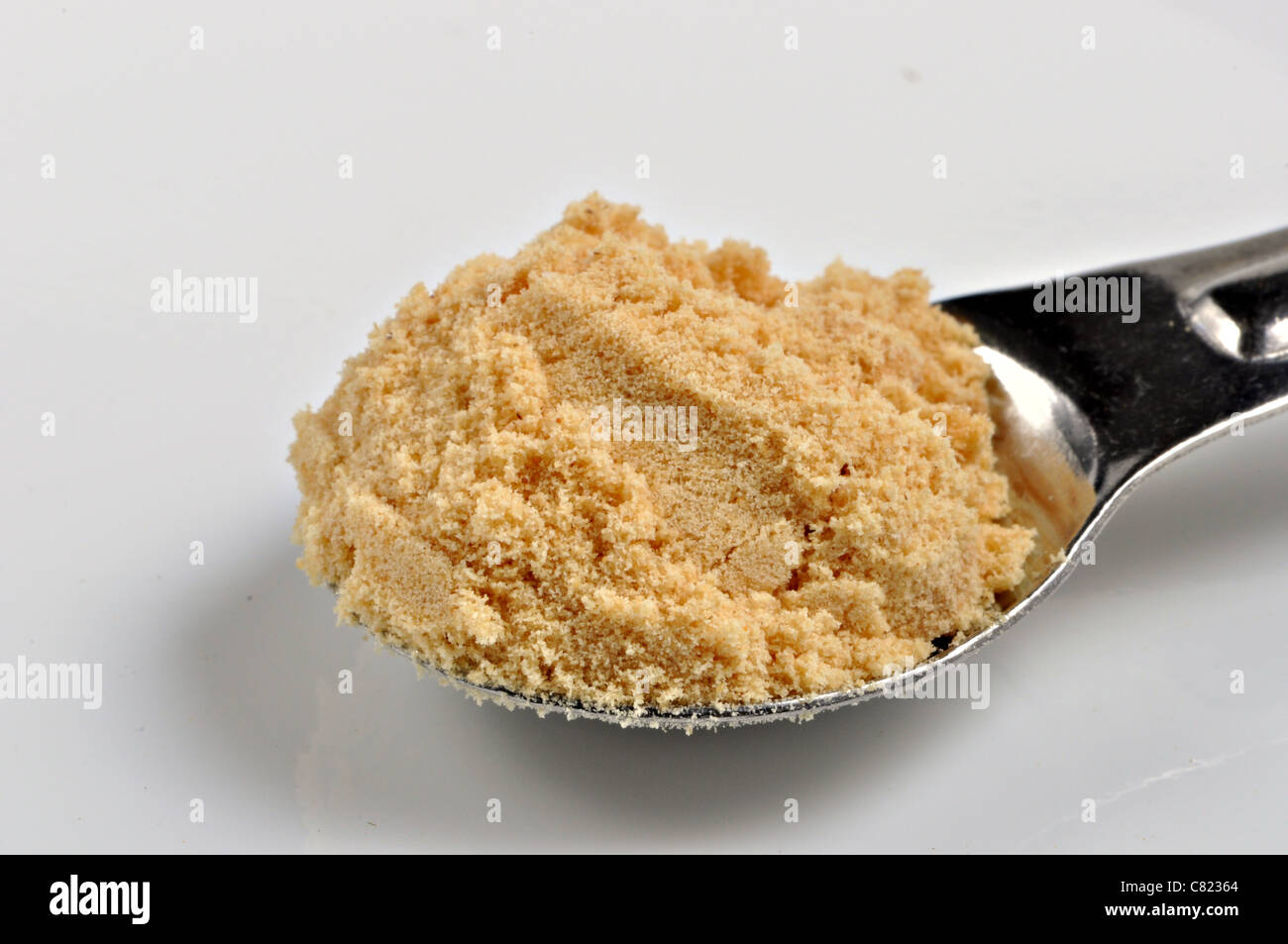 A spoonful of ground double superfine mustard sits on a white background. Stock Photo