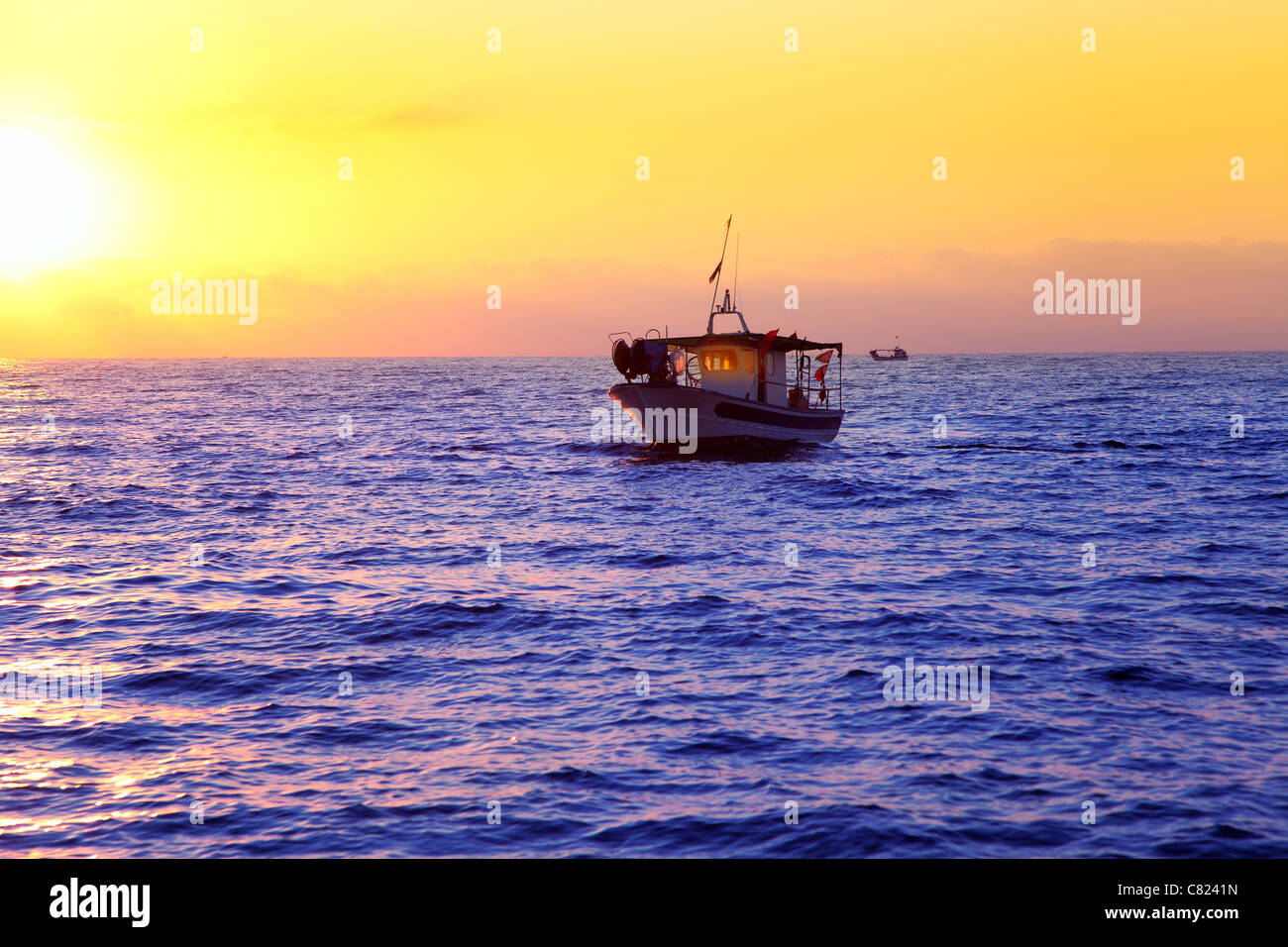 blue sea sunrise with sun in horizon with fishing boat sailing Stock Photo