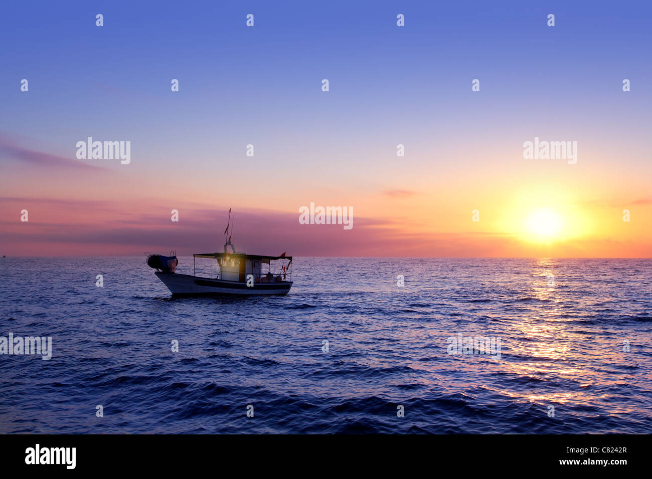 blue sea sunrise with sun in horizon with fishing boat sailing Stock Photo