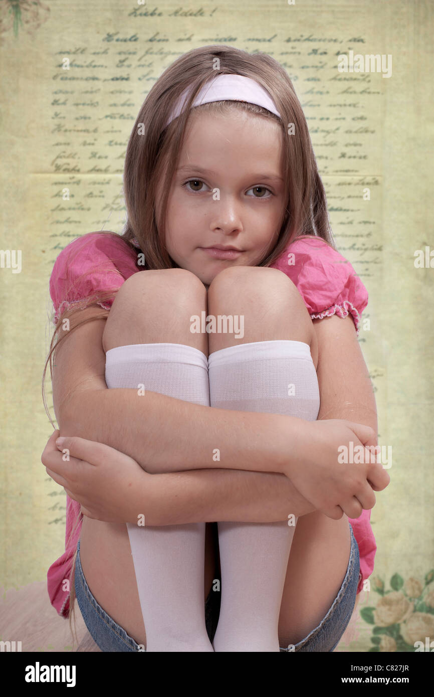 seated girl looks dreamily into the camera, with old letter as a background Stock Photo