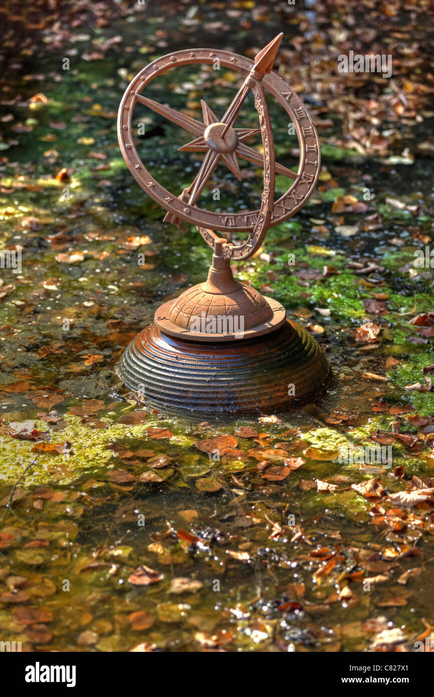 an old sundial in a pond with autumn leaves Stock Photo