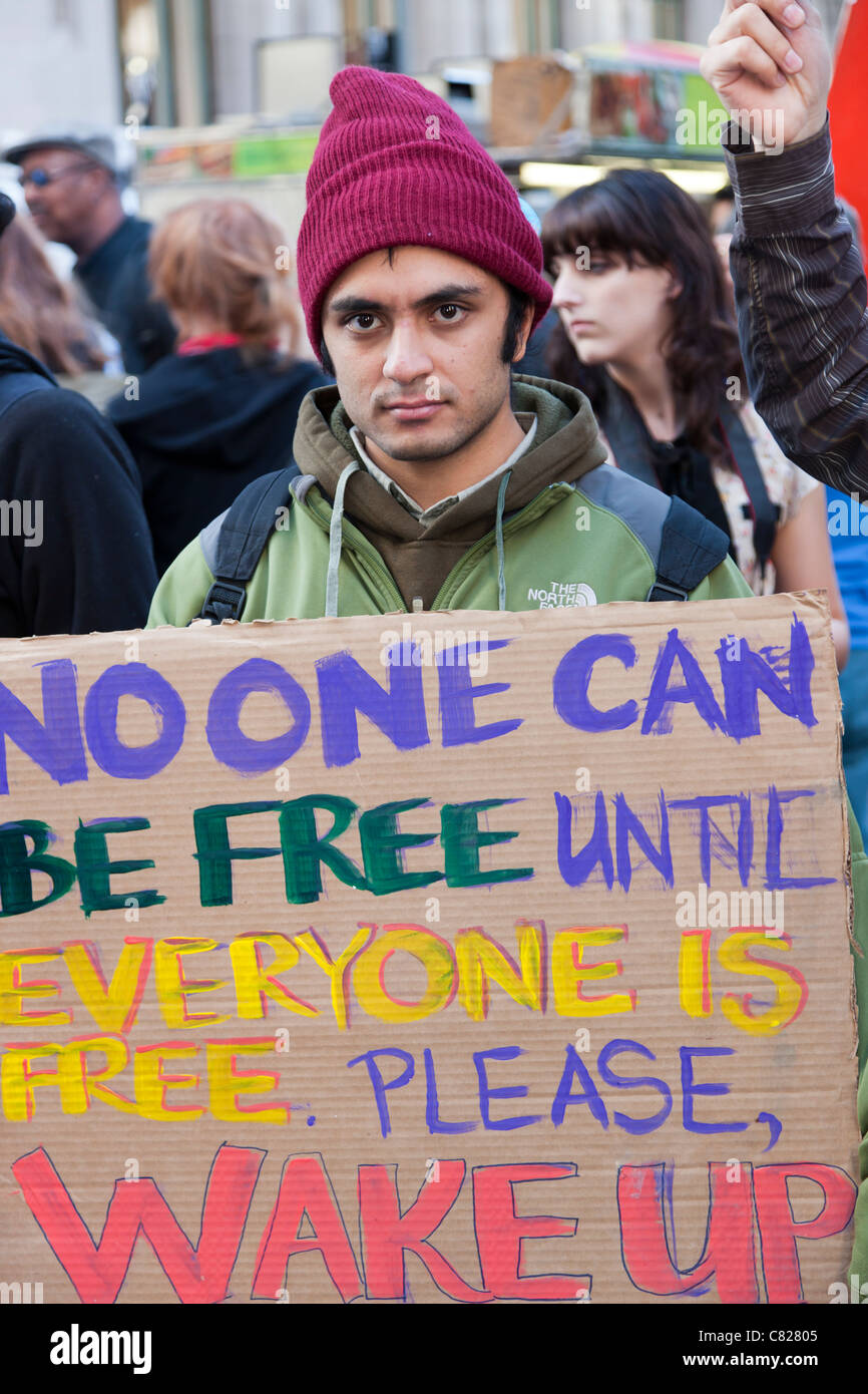 A man holds a protest sign reading 'No one can be free until everyone is free.  Please, Wake up' during the Occupy Wall Street Stock Photo