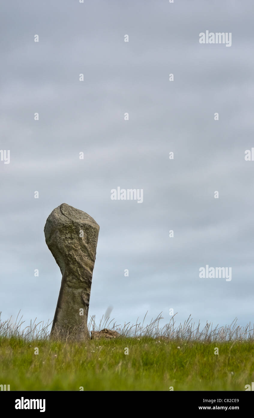 Single, fist-shaped, standing stone against grey sky Stock Photo