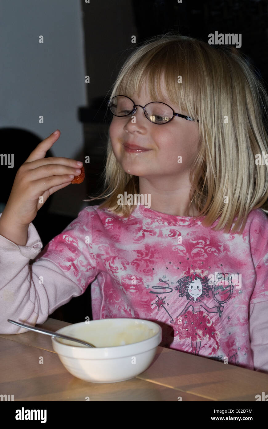 Little Blond Girl wearing a pink shirt admiring a strawberry Stock