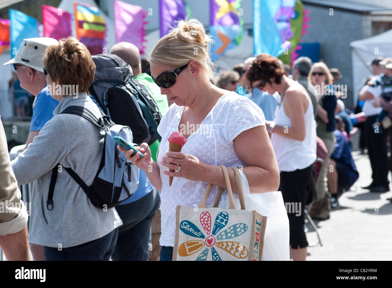 Cornwall, UK - Woman eating ice cream while using mobile phone Stock Photo