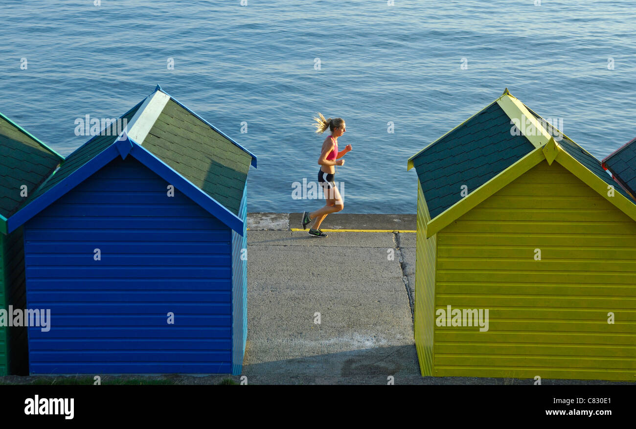 Colourful, colorful seaside huts or beach chalets with female jogger at Whitby, Yorkshire, England. Stock Photo