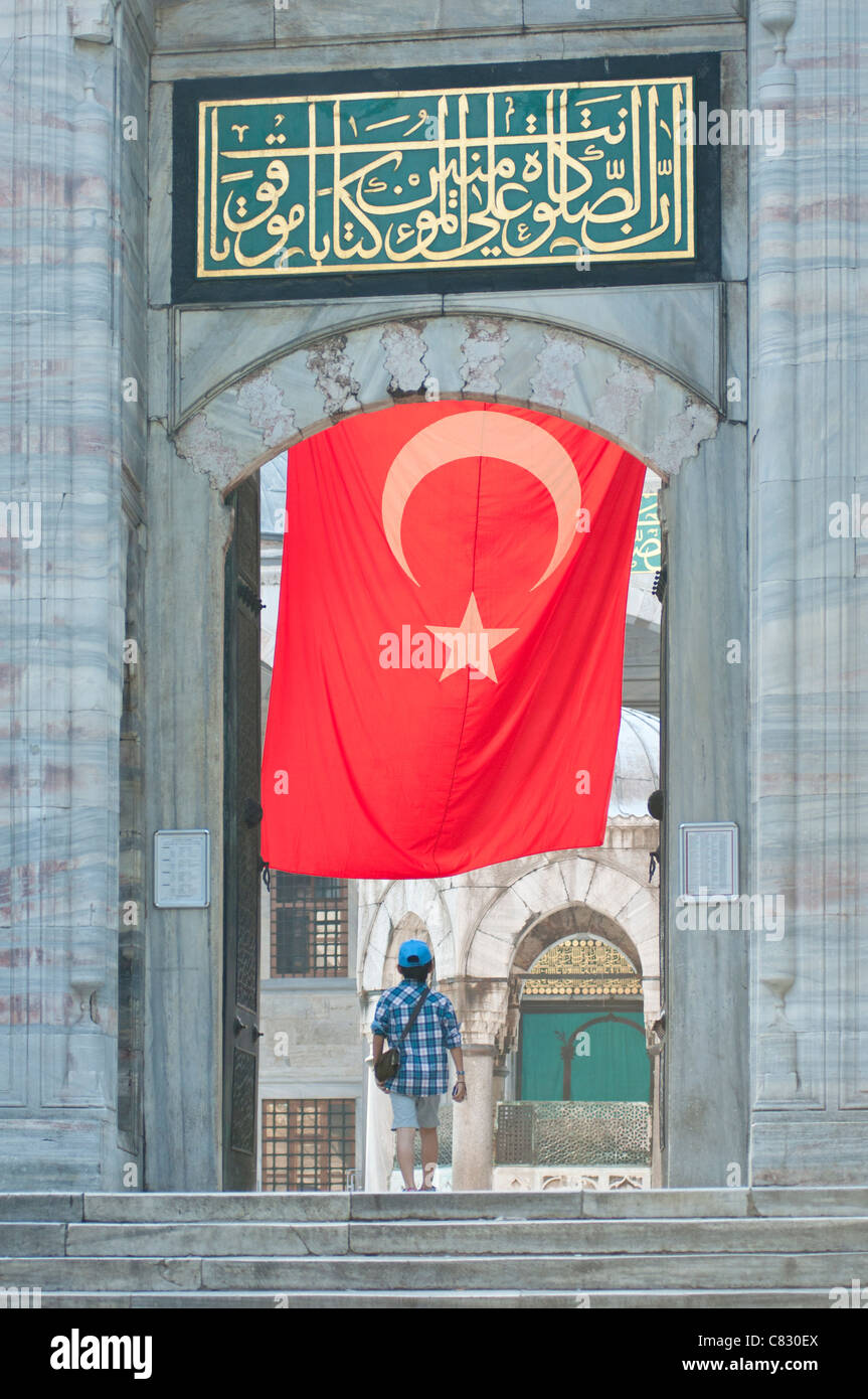 A visitor to the Blue mosque in Istanbul with large Turkish flag hanging overhead. Stock Photo