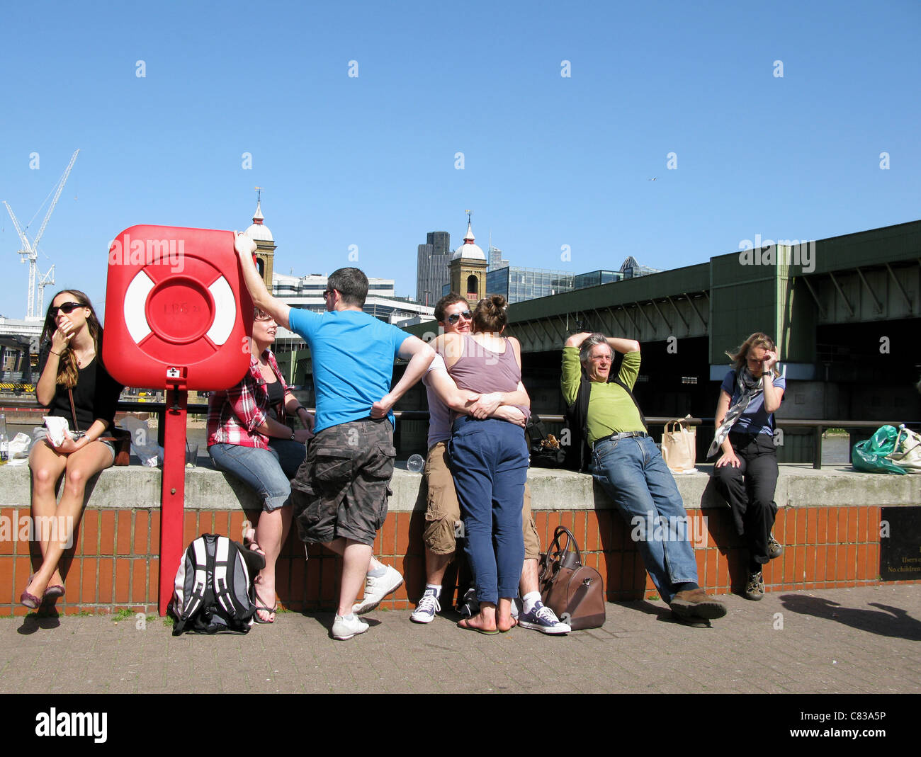 People sitting on wall by the Thames London UK Stock Photo