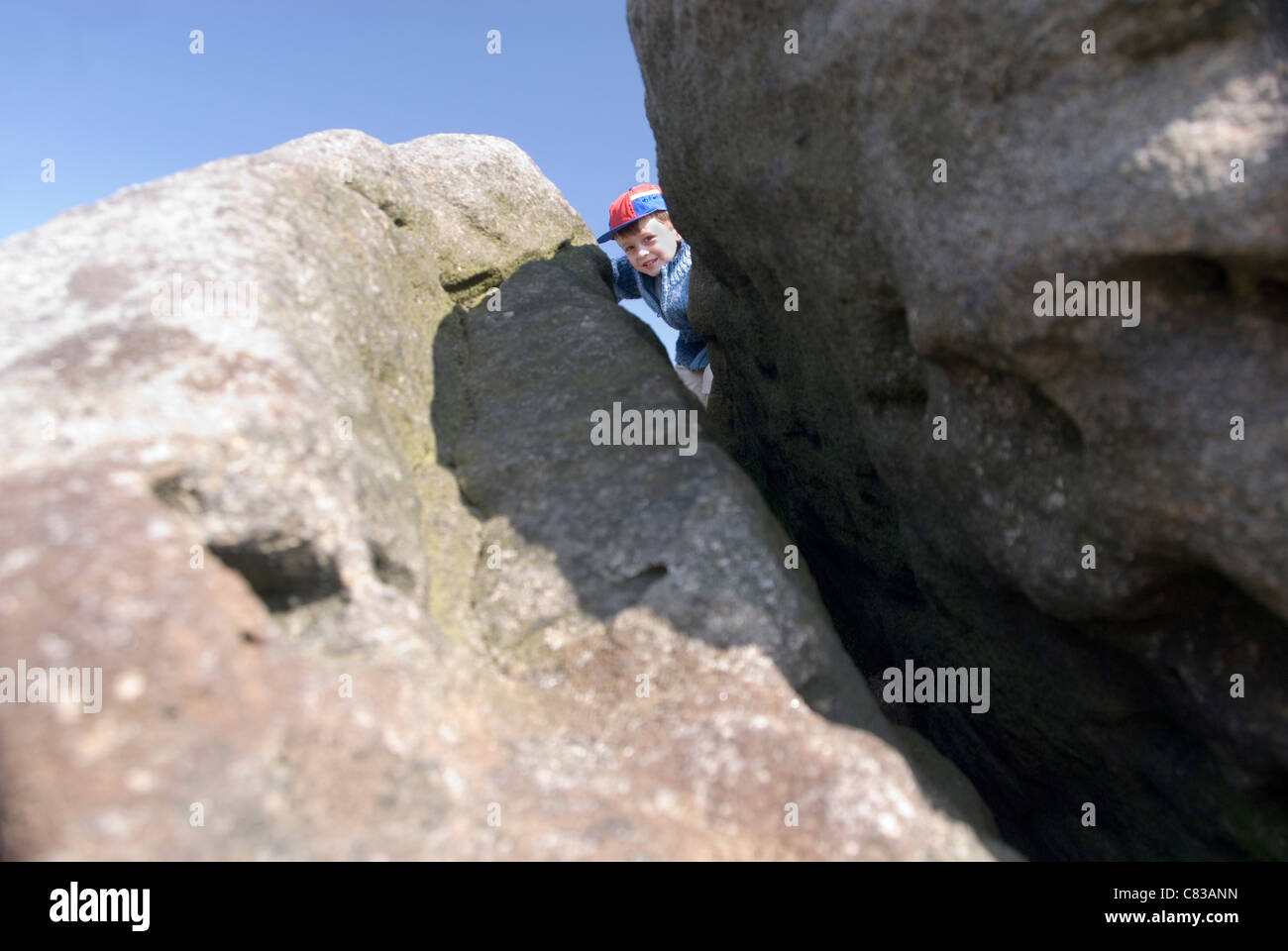 Little Boy Peaking though Crack in Giant Boulder Rock on Top of Millstone Edge, nr Surprise View, Peak District, UK Stock Photo