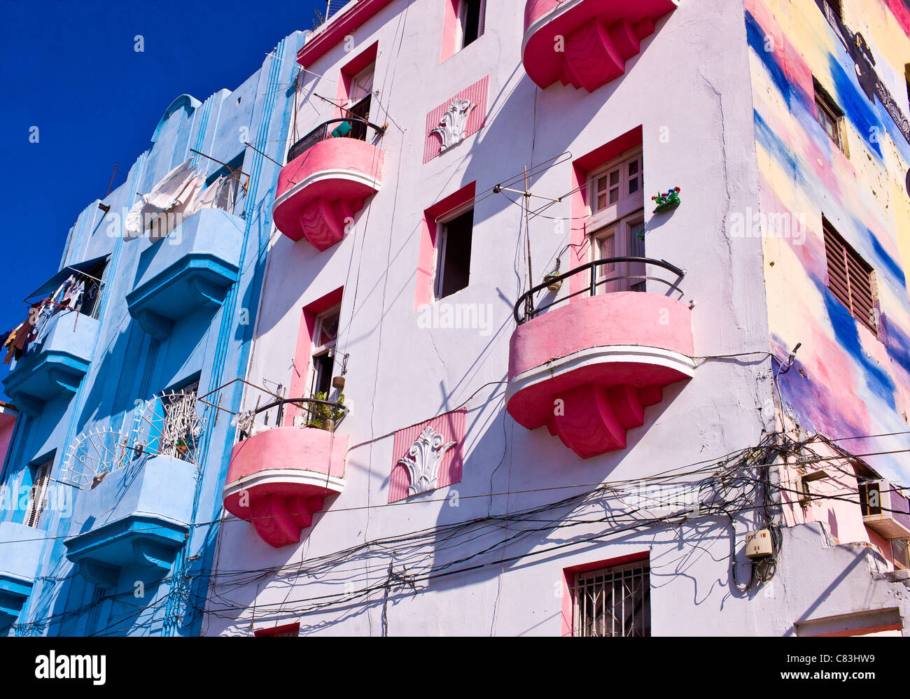 Exterior  building in Havana painted in many shades of blue, yellow and pink. Electrical and telephone wires run on the walls. Stock Photo