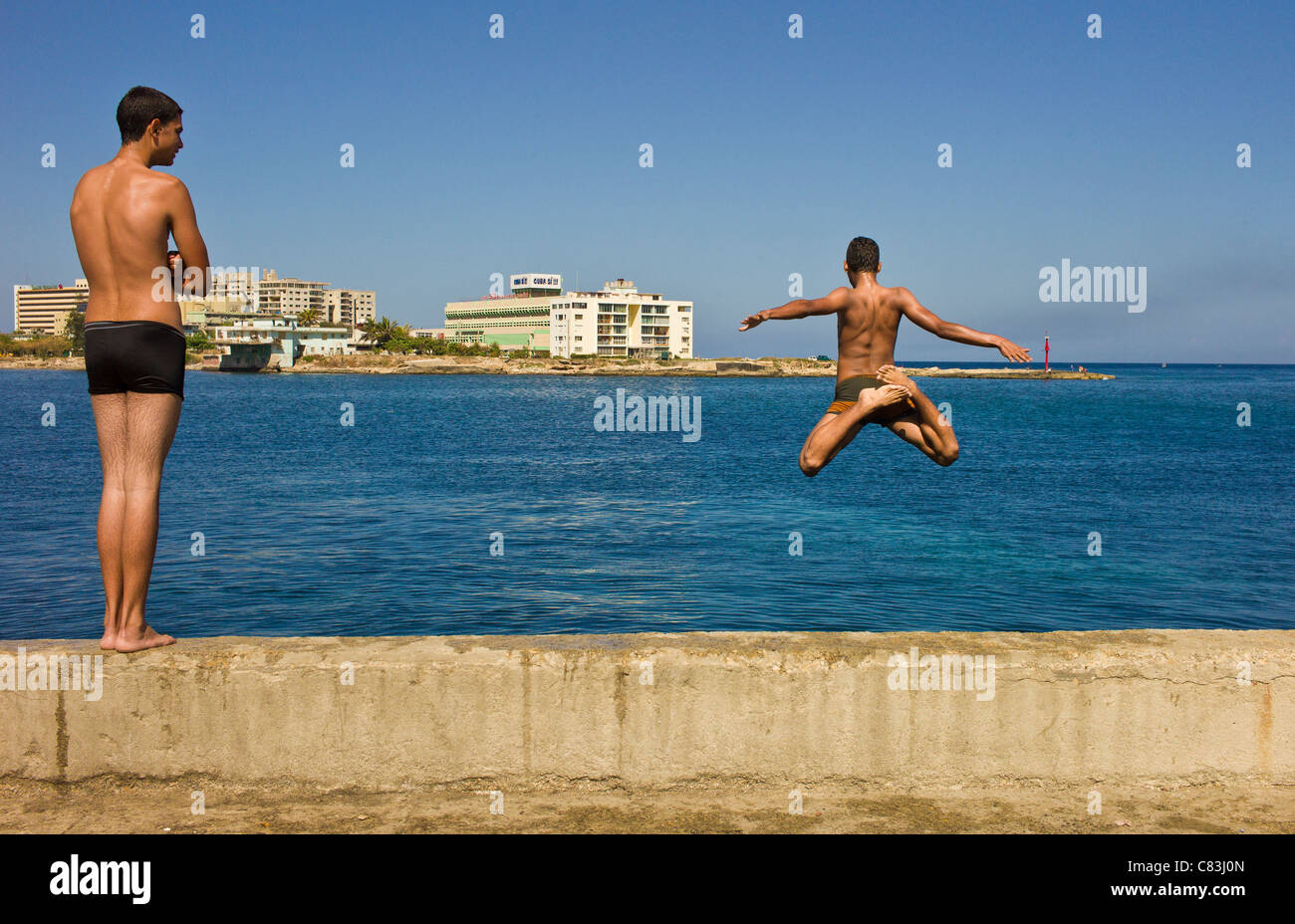 To escape the everpresent heat, two teenage boys are jumping into Bahia de la Habana on a sunny day along the Malecon in Havana. Stock Photo