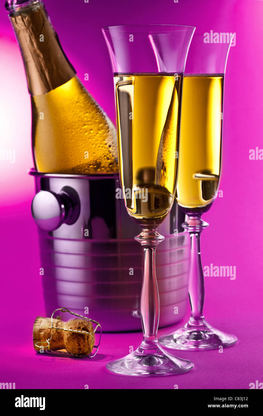 Champagne bottle in cooler and two champagne glasses. Isolated on a pink background. Stock Photo