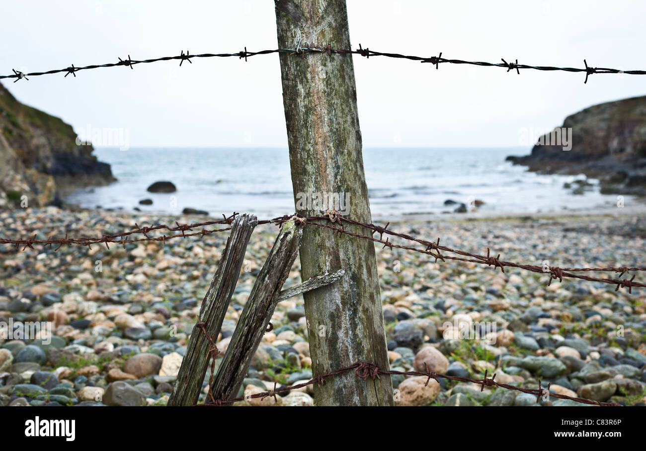 Barbed wire fence on rocky beach Stock Photo