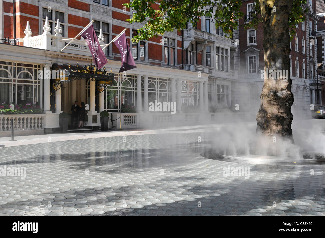 Street scene steam mist vapour cloud on 'Silence’ water feature rising from tree trunk  Carlos Place Mayfair Connaught Hotel beyond London West End UK Stock Photo