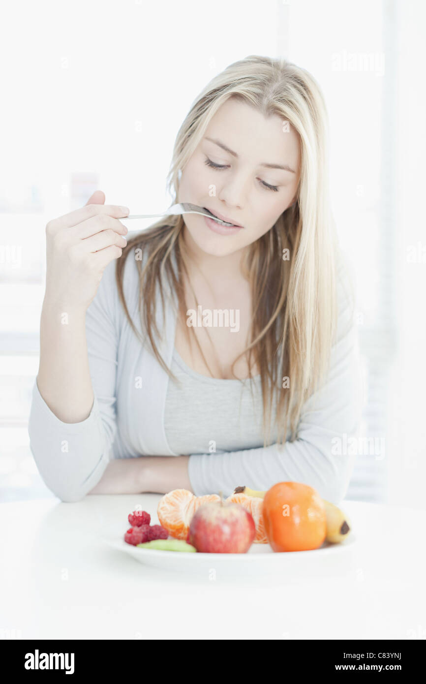 Smiling woman eating plate of fruit Stock Photo