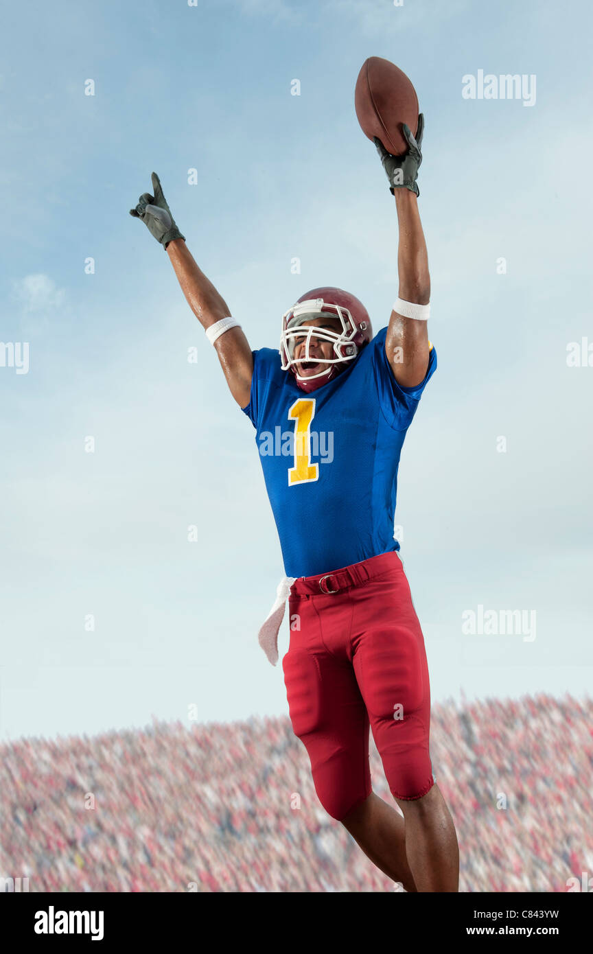 Mixed race football player with arms raised holding football Stock
