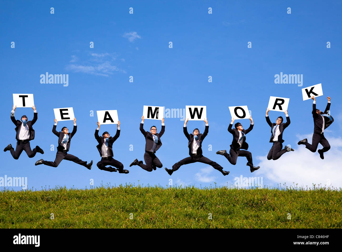 happy businessman holding teamwork text and jumping on the green field Stock Photo