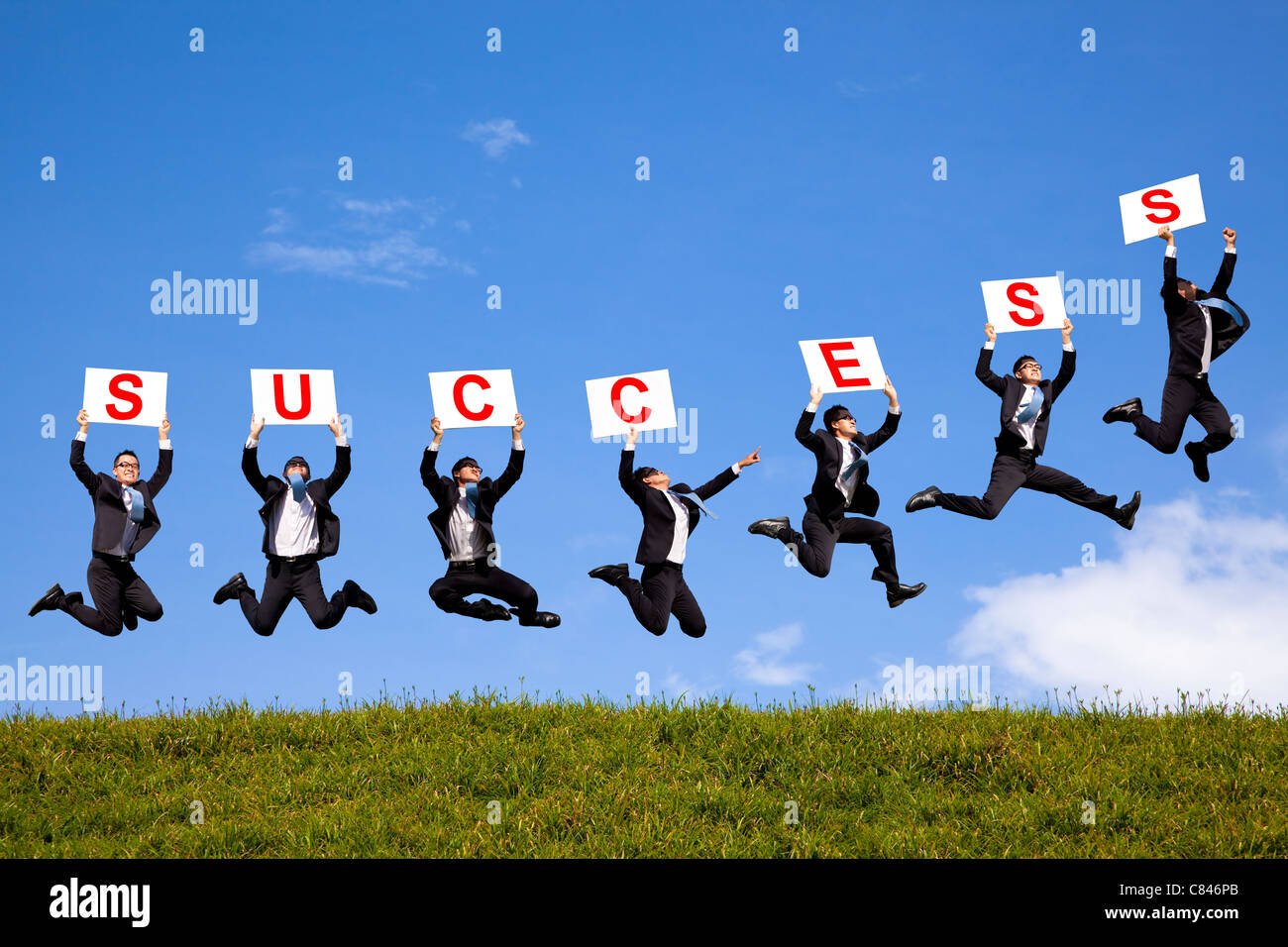 happy businessman holding success text and jumping on the green field Stock Photo