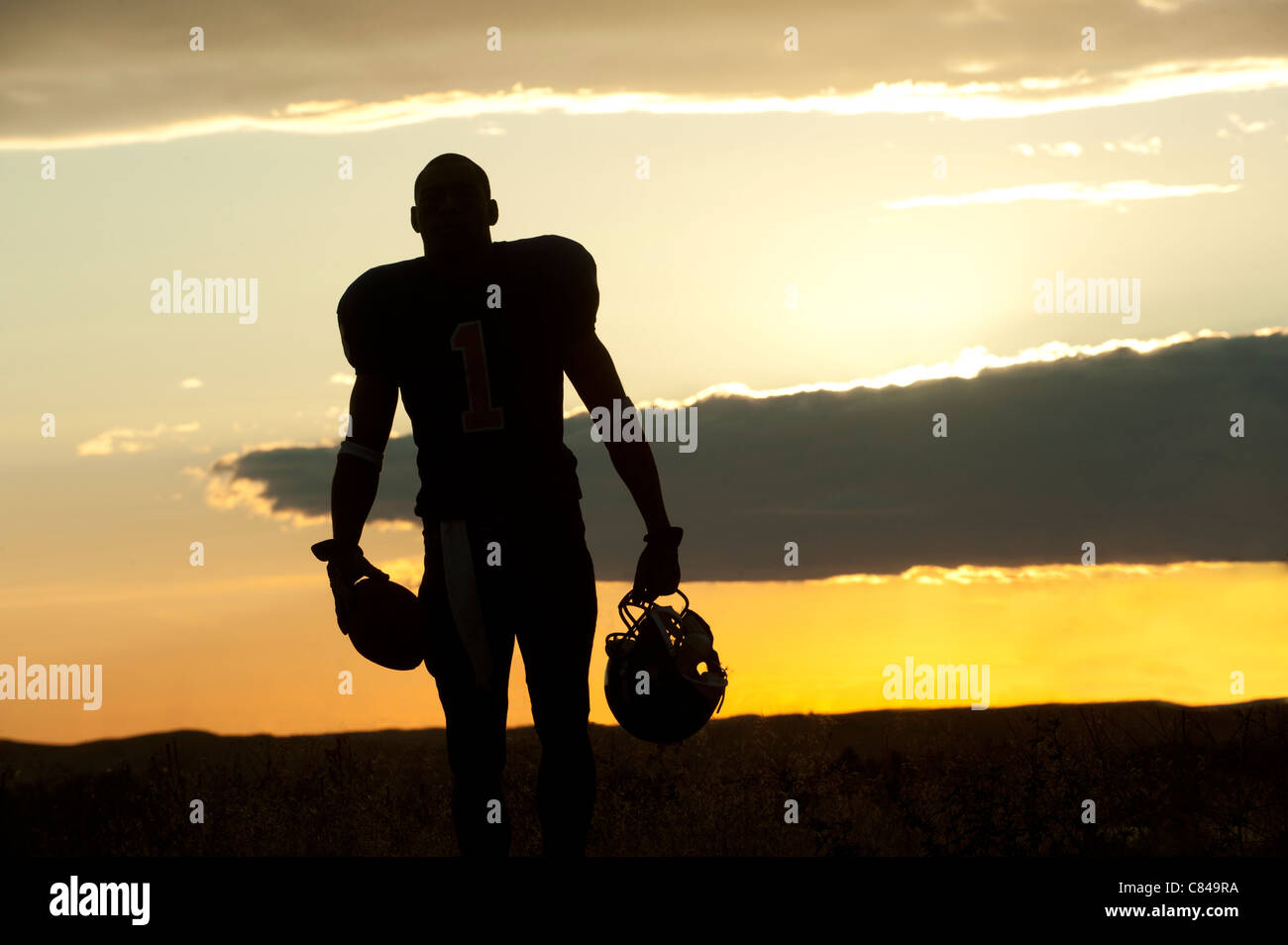 Silhouette of Black football player carrying helmet and football Stock Photo
