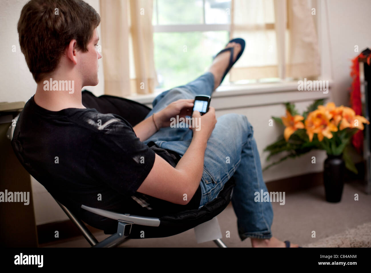Caucasian man text messaging on cell phone in dorm room Stock Photo