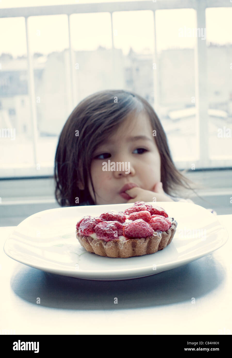 Little girl licking finger, raspberry tart in front Stock Photo
