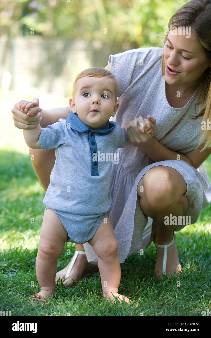 Mother helping baby stand outdoors Stock Photo