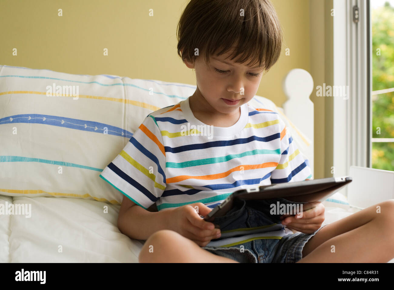 Boy sitting on bed, using digital tablet Stock Photo