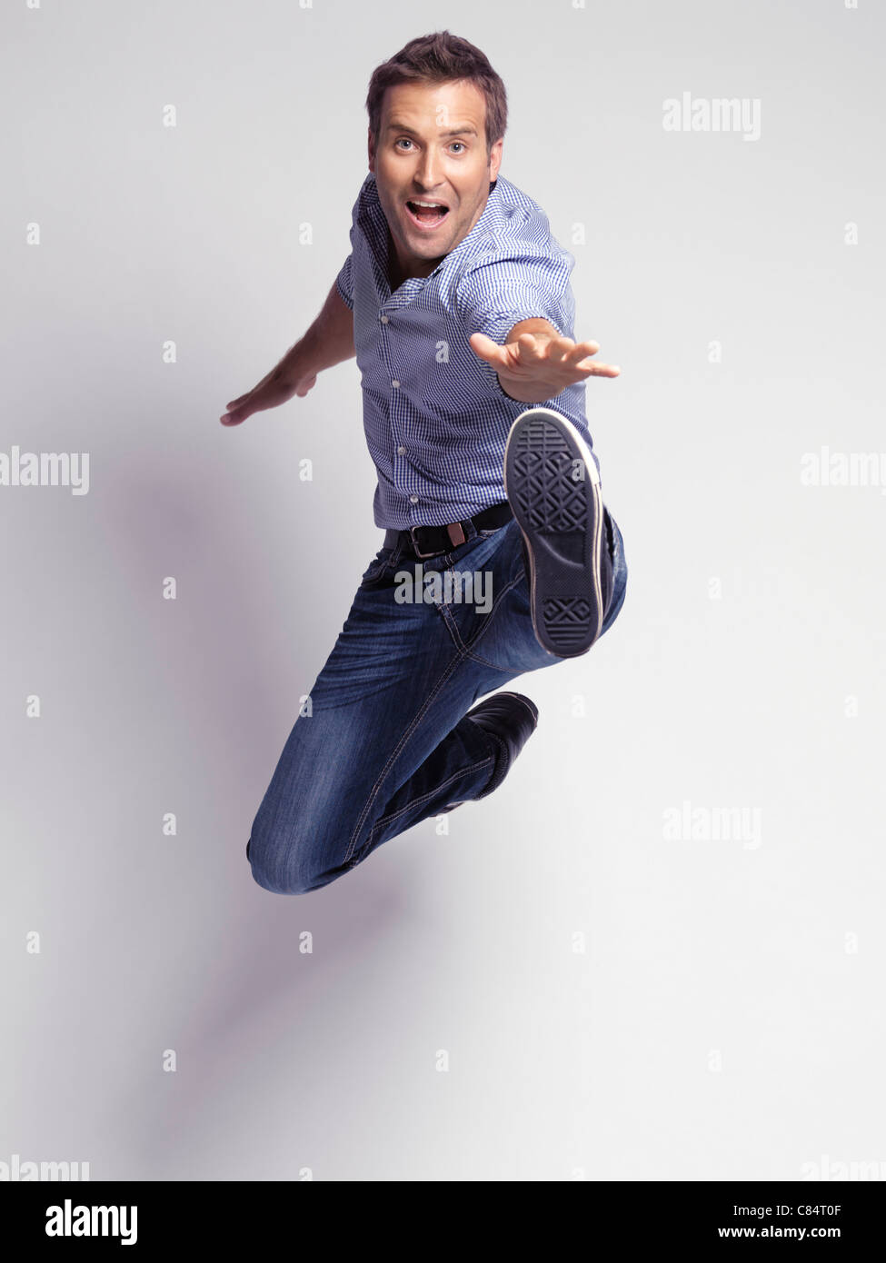 Happy jumping young man wearing jeans and a shirt isolated on gray