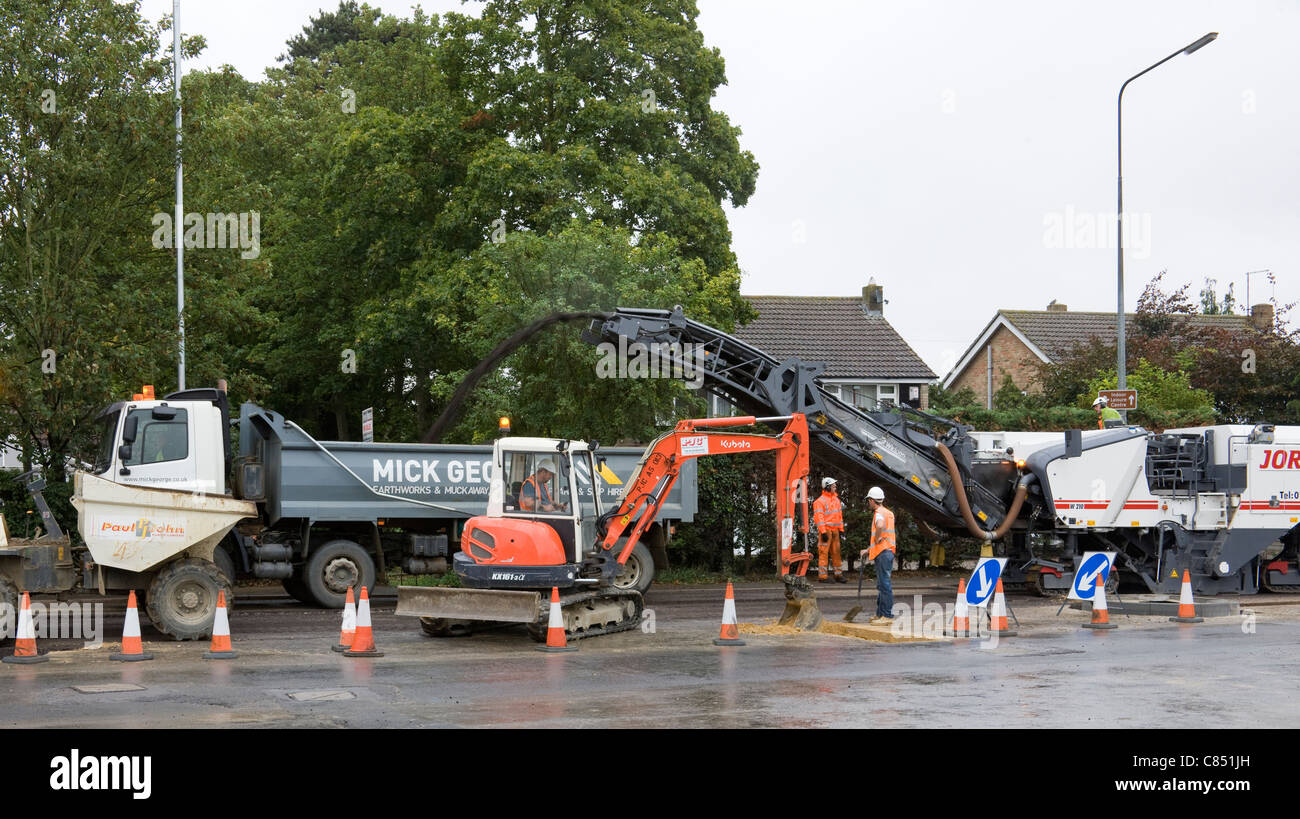 Old road surface being stripped by a planer, the resulting old tarmac is then being poured into the back of a lorry. Stock Photo