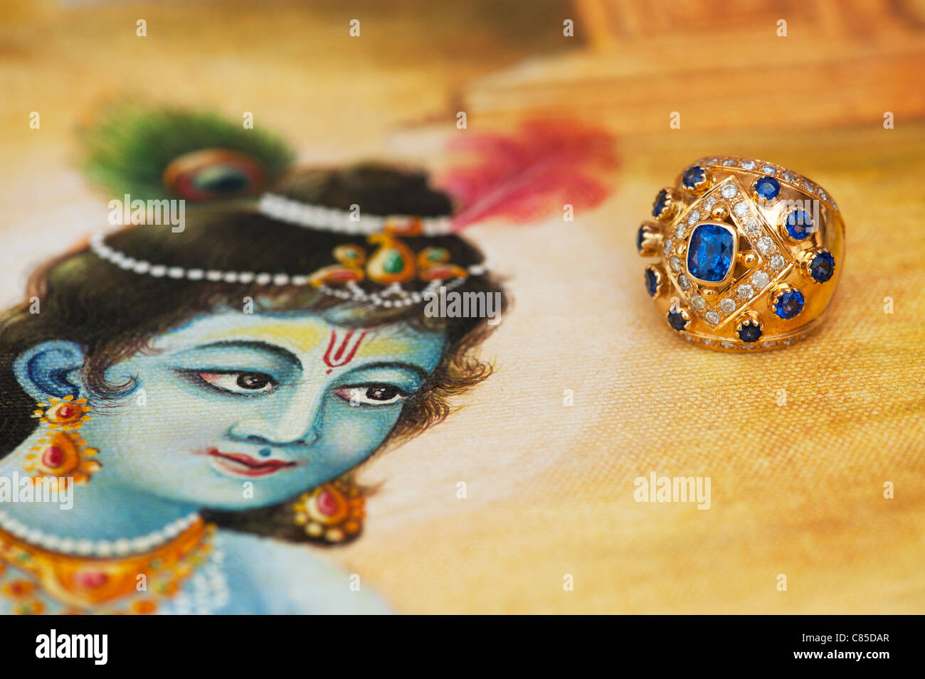 Indian Blue sapphire and diamond gold ring on a Traditional Indian oil painting of Lord Krishna Stock Photo