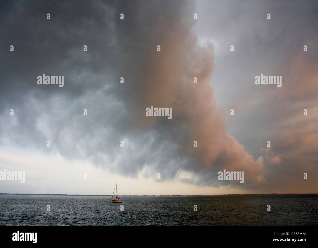 A dramatic cloud heralds the passing of a weather front as it passes over a bay and a moored sailboat. Stock Photo