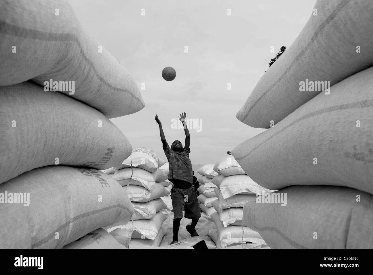 Young internally displaced boy playing happily with a football amid large sacks of basic foodstuff at World Food Programme WFP distribution point in North Kivu, DR Congo central Africa Stock Photo