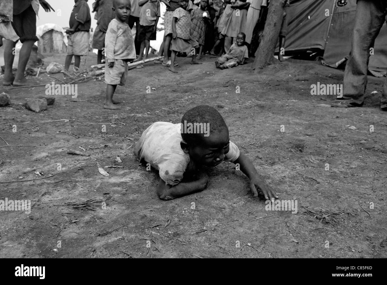 Young boy crawls on the ground and cries in a camp for internal displaced people in North Kivu province in DR Congo Africa Stock Photo