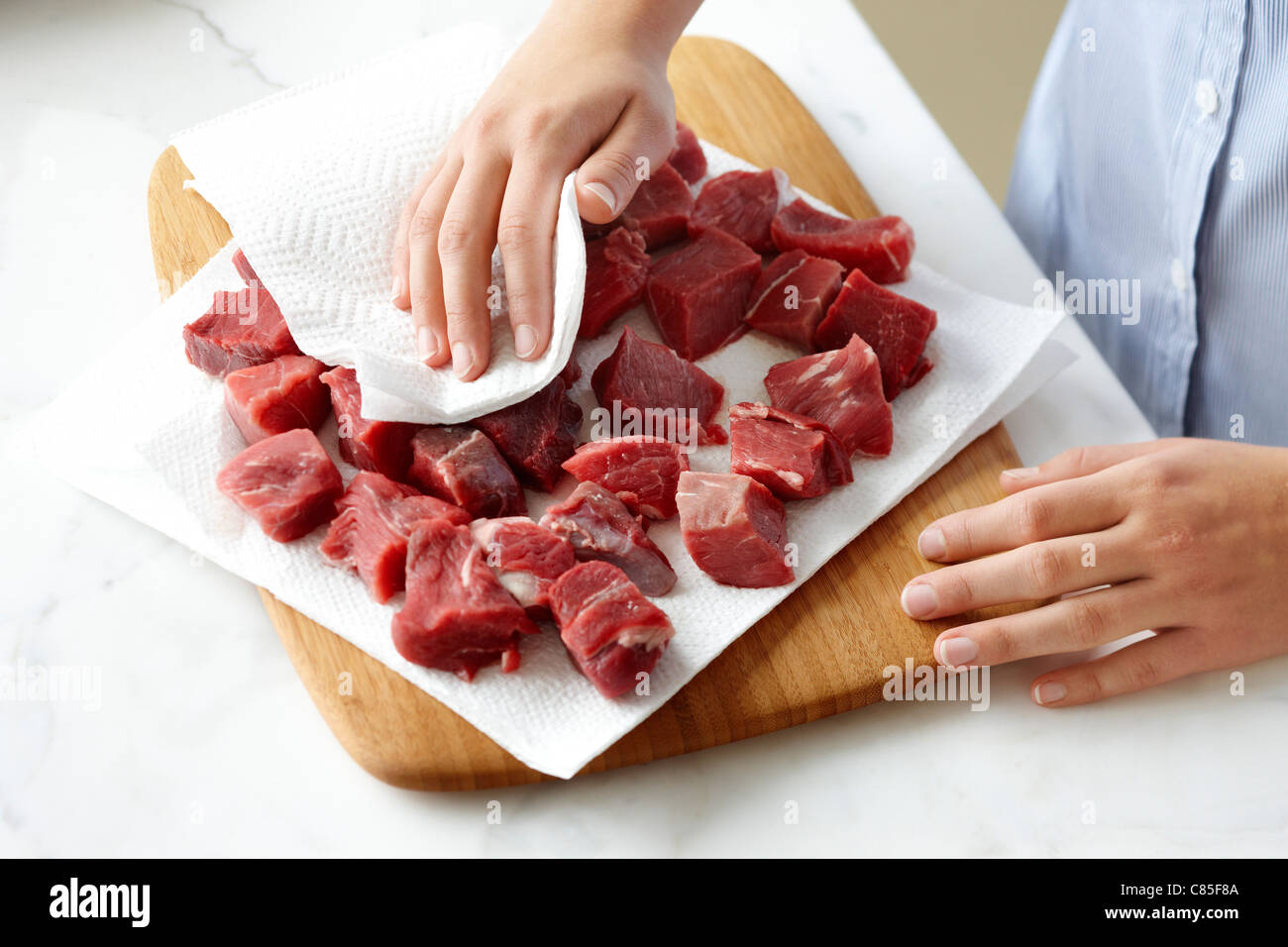 Woman using Paper Towel to dry Beef Cubes Stock Photo