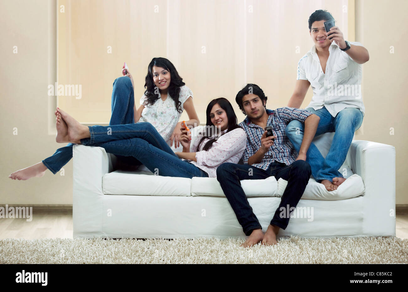 Youngsters with mobile phones sitting on a sofa Stock Photo