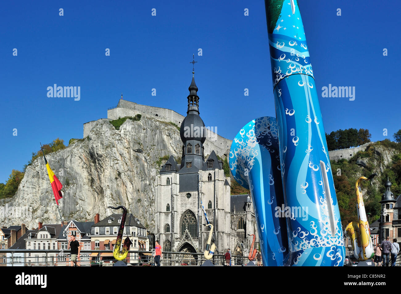Painted saxophone and the Collegiate Church of Notre-Dame along the river Meuse at Dinant, Belgium Stock Photo