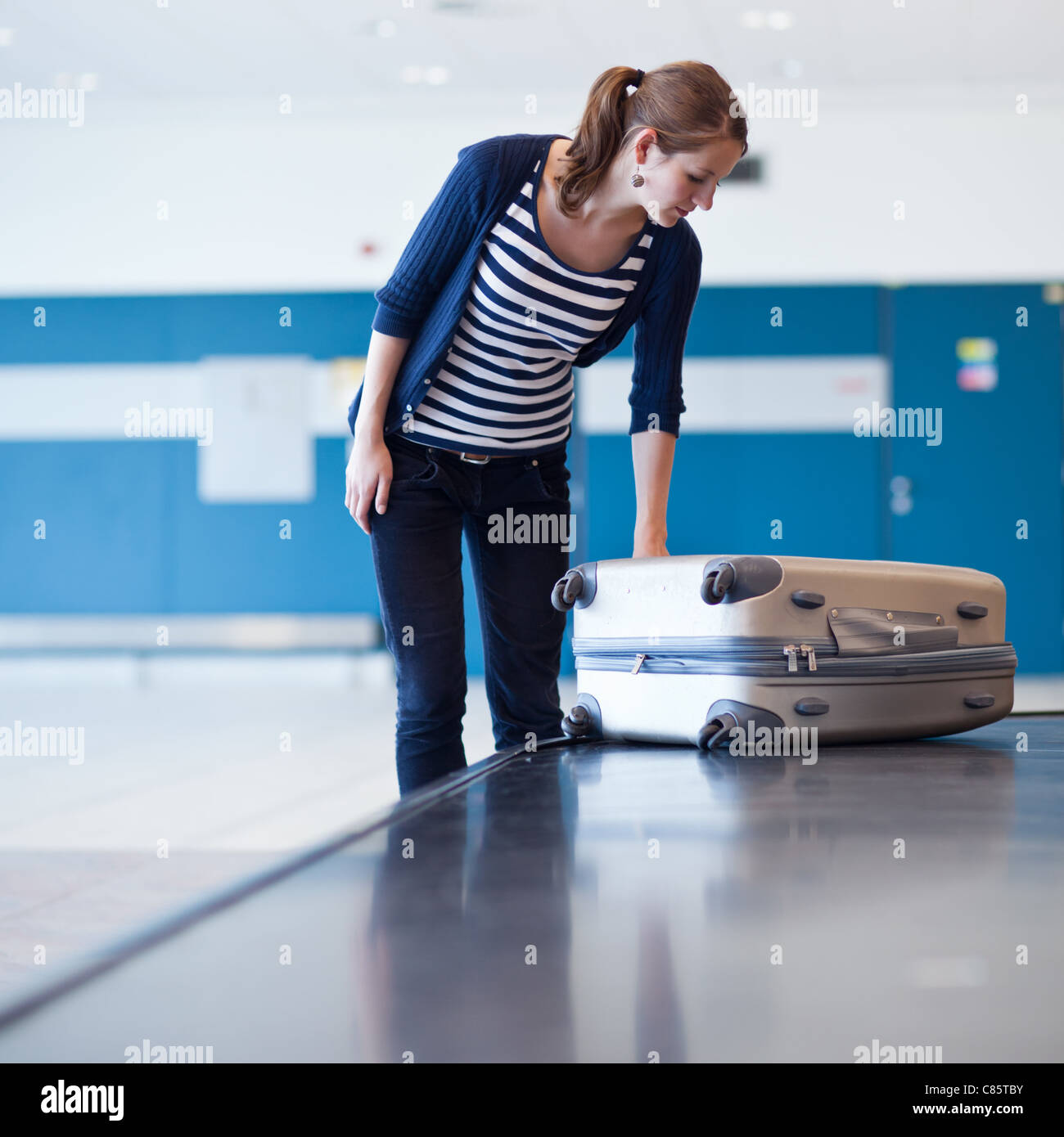 Baggage claim at the airport - pretty young woman taking her suitcase off the baggage carousel (color toned image) Stock Photo