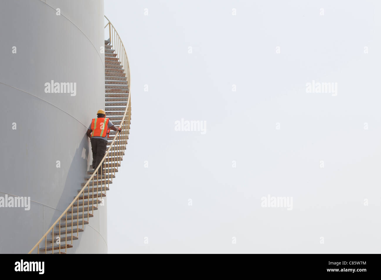 Mixed race worker climbing staircase on storage tank Stock Photo