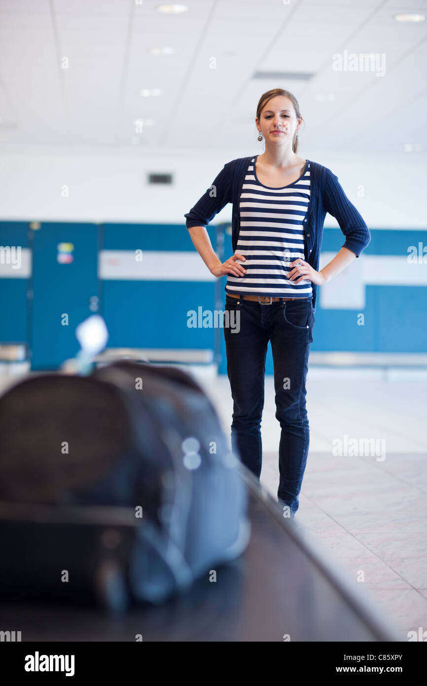 Baggage claim at the airport - pretty young woman taking her suitcase off the baggage carousel (color toned image) Stock Photo