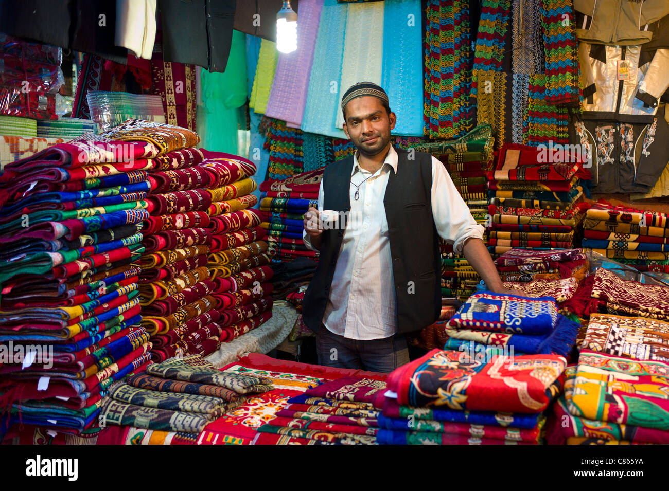 Stallholder drinking chai in shop selling prayer mats at muslim Meena Bazar, in Old Delhi, India Stock Photo