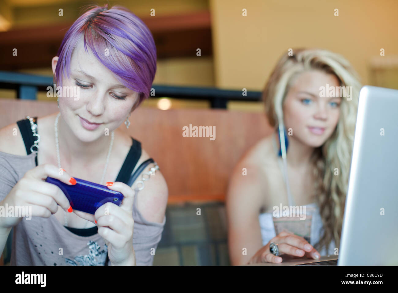 Two teen girls in  coffee house on smart phone and  laptop Stock Photo
