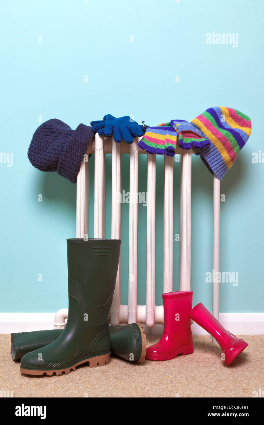 Photo of childrens hats, gloves and wellies boots drying by an old traditional cast iron radiator in the hallway, Stock Photo
