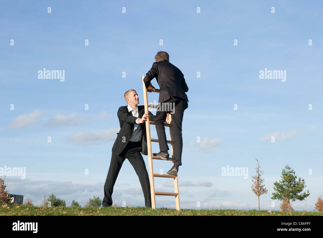 Businessman holding ladder for colleague Stock Photo Alamy