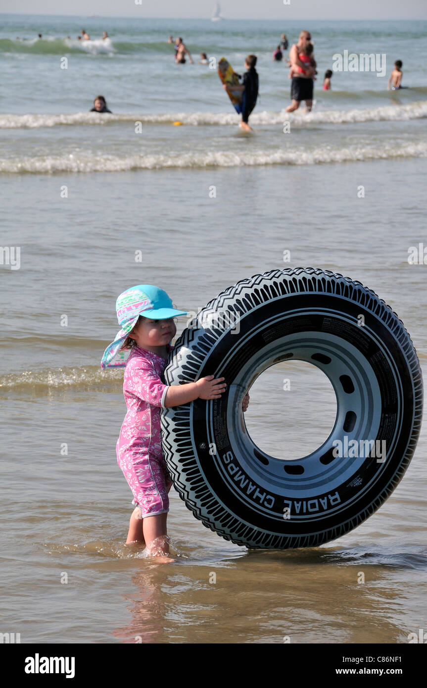 Toddler dressed in sun protective clothing holding onto very large rubber  ring in sea and on beach at West Wittering,West Sussex, England, UK Stock  Photo - Alamy