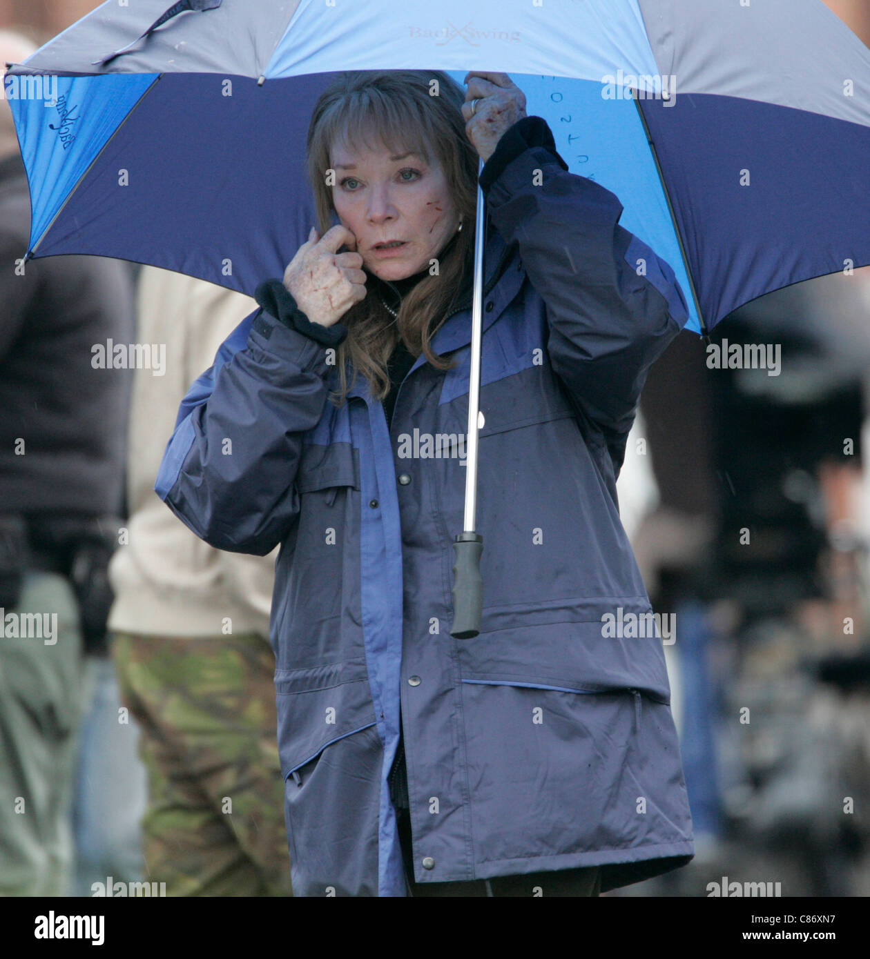 Shirley MacLaine shelters from the rain under an umbrella on location