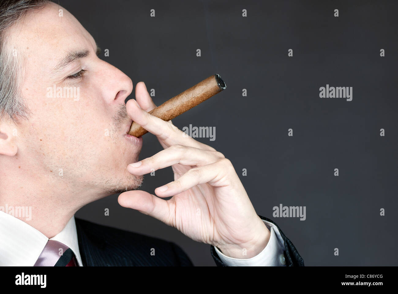 Close-up of a businessman smoking a cigar appreciatively. Stock Photo